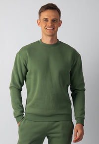 A man wearing a green Hudson lounge sweatshirt and matching pants, standing against a plain background.